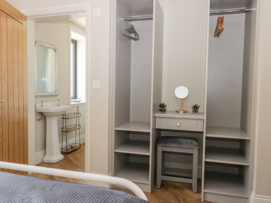 A bedroom with an open closet containing hangers a vanity table with a mirror and stool and a view into a bathroom with a pedestal sink and mirror at Pheasant's Roost in Lelley near Burton Pidsea