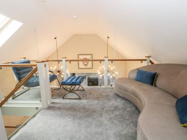 A loft area with a curved sofa and blue chair with footrest overlooking a kitchen at Pheasant's Roost in Lelley near Burton Pidsea