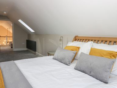 A bedroom with a wooden bed frame white and gray bedding and yellow pillows at Pheasant's Roost in Lelley near Burton Pidsea