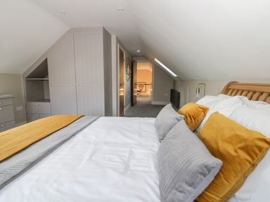 A bedroom with a bed with yellow and gray pillows a wooden headboard built in wardrobes and a door leading to another room at Pheasant's Roost in Lelley near Burton Pidsea