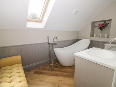A bathroom with a white freestanding bathtub under a skylight and a yellow bench at Pheasant's Roost in Lelley near Burton Pidsea