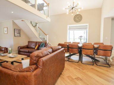 An open living and dining room with brown leather sofas a wooden dining table with chairs and a staircase with glass railing at Pheasant's Roost in Lelley near Burton Pidsea