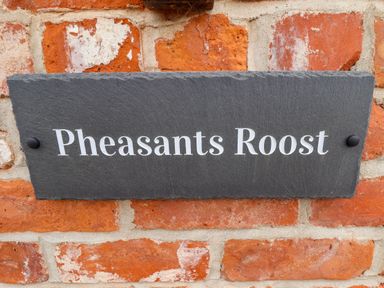 A black slate house name sign on a red brick wall with the text Pheasants Roost at Pheasant's Roost in Lelley near Burton Pidsea