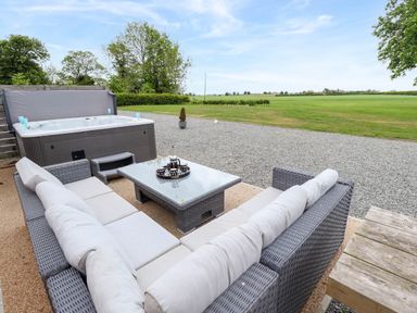 An outdoor patio with a hot tub, wicker sofas with cushions and a glass top coffee table at Pheasant's Roost in Lelley near Burton Pidsea