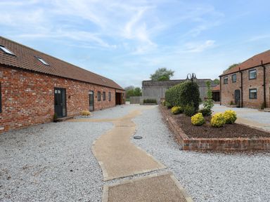 A courtyard with gravel, a pathway, brick buildings, and a garden area with shrubs at Pheasant's Roost in Lelley near Burton Pidsea