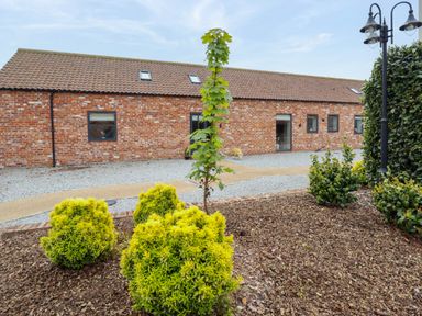 A brick building with multiple windows and a gravel pathway surrounded by bushes and a lamp post at Pheasant's Roost in Lelley near Burton Pidsea