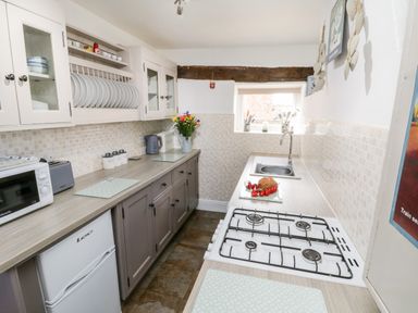A narrow kitchen with gas stove sink microwave flowers and cabinets at The Lodge in Stainsacre near Whitby