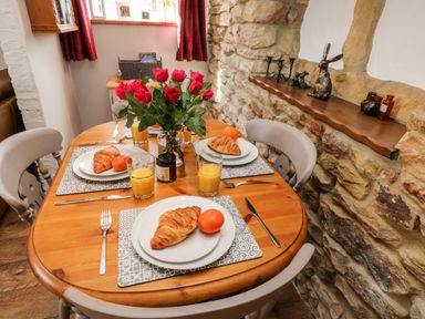 A dining table set with croissants oranges glasses of orange juice and a vase of red roses in a room with stone wall and wooden shelf at The Lodge in Stainsacre near Whitby