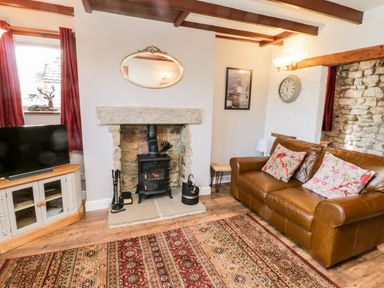 A living room with leather sofa and floral cushions fireplace and TV on a cabinet at The Lodge in Stainsacre near Whitby