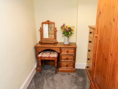A small wooden dressing table with a mirror and a vase with flowers and a cushioned stool next to a wooden wardrobe at The Lodge in Stainsacre near Whitby