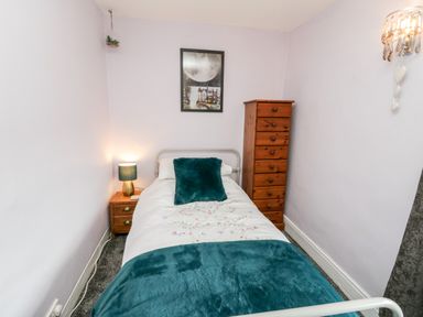 A small bedroom with a single bed blue pillows and blanket a wooden nightstand with lamp and a tall wooden chest of drawers at The Lodge in Stainsacre near Whitby