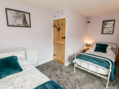 A bedroom with two single beds a wooden door and framed pictures on the walls at The Lodge in Stainsacre near Whitby