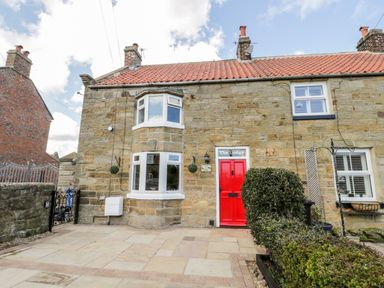 A stone house with a red door and bay windows at The Lodge in Stainsacre near Whitby