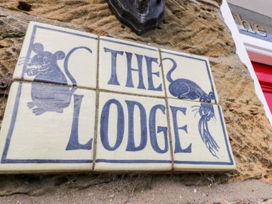 A sign made of tiles with the words The Lodge and drawings of two mice on a stone wall at The Lodge in Stainsacre near Whitby