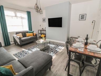 A living room with grey sofas a dining table set with plates and glasses and a wall mounted TV at Pebble Cove in Amble