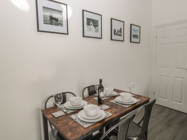 A dining table set with four place settings and a bottle of wine under framed photographs on the wall at Pebble Cove in Amble
