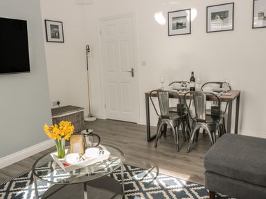 A dining table set with plates and wine glasses and a coffee table with yellow flowers in a living room at Pebble Cove in Amble