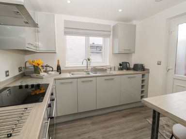 A kitchen with grey cabinets a sink under a window a stove kettle toaster and a table at Pebble Cove in Amble