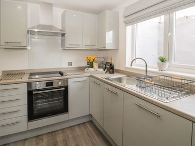 A kitchen with oven stove sink drying rack and window at Pebble Cove in Amble