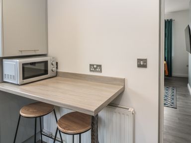 A kitchen counter with a microwave and two stools next to a radiator at Pebble Cove in Amble