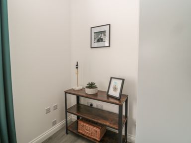 A corner with a dark wood and metal shelving unit holding a lamp plant and framed picture at Pebble Cove in Amble