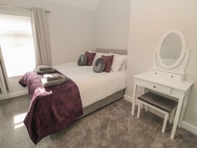 A bedroom with a bed with pillows and towels and a white dressing table with a mirror at Pebble Cove in Amble