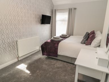 A bedroom with a bed folded towels a wall-mounted television a radiator and a white dressing table at Pebble Cove in Amble