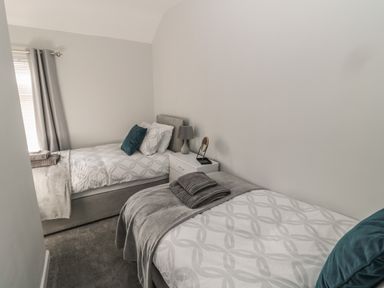 A bedroom with two single beds a nightstand with a lamp and mirror and folded towels on beds at Pebble Cove in Amble