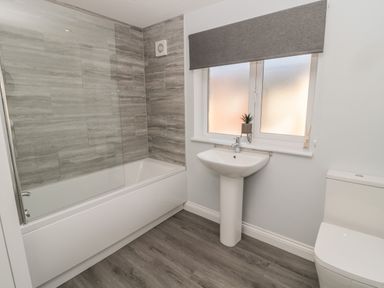 A bathroom with a bathtub shower combo sink toilet and window with a plant at Pebble Cove in Amble