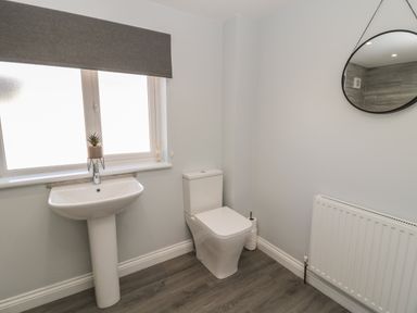 A bathroom with a pedestal sink a toilet a round mirror and a radiator at Pebble Cove in Amble