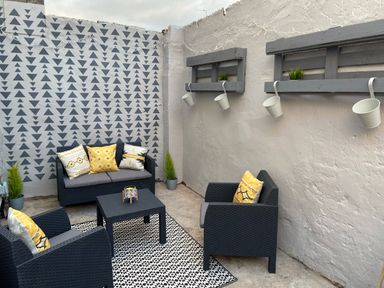 An outdoor patio with black wicker chairs and sofa with yellow and white cushions a black table a patterned rug and potted plants at Pebble Cove in Amble