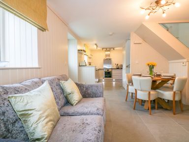 A living room with a sofa and cushions opening to a kitchen and dining area with a table set for four at Apple Barn in Crantock