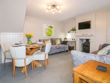 A living room with two sofas a wooden dining table with chairs a fireplace and a wall-mounted television at Apple Barn in Crantock