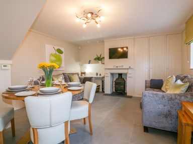 A dining and living area with a round table set with plates and glasses a sofa and a fireplace at Apple Barn in Crantock