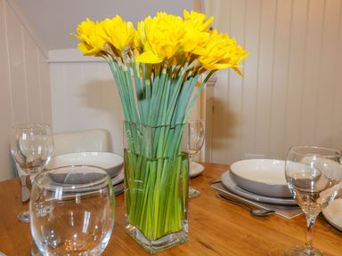 A dining table with a vase of yellow flowers and glassware at Apple Barn in Crantock