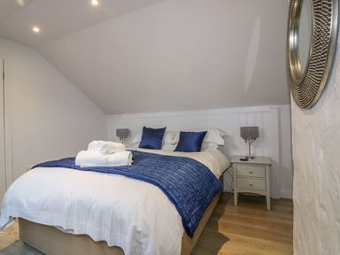 A bedroom with a double bed blue pillows blue throw towels on bed bedside tables and lamps at Apple Barn in Crantock