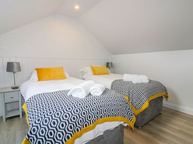 A bedroom with two single beds with yellow pillows and patterned blankets at Apple Barn in Crantock