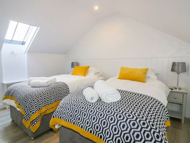 A bedroom with two single beds with patterned covers and yellow cushions at Apple Barn in Crantock