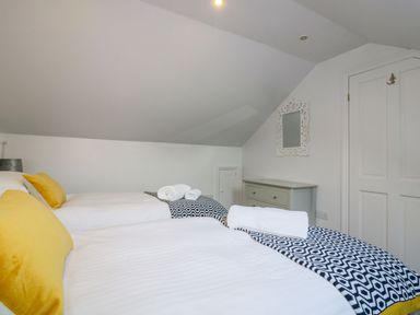 A bedroom with two single beds with yellow pillows and patterned blankets at Apple Barn in Crantock