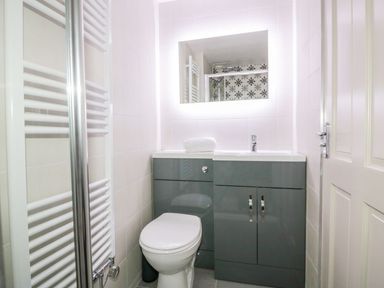 A bathroom with a toilet sink cabinet and illuminated mirror at Apple Barn in Crantock