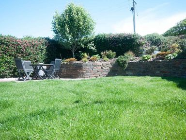 A garden with a lawn table and chairs by a stone wall and hedges at Apple Barn in Crantock