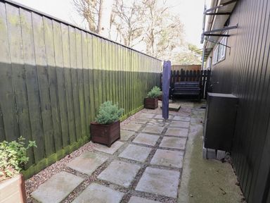 A narrow outdoor patio area with paving stones and wooden planters along a wooden fence at 98 Cherry Park in Chapel St Leonards