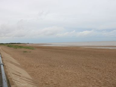 A sandy beach with some grass near a concrete promenade and the sea in the distance at 98 Cherry Park in Chapel St Leonards