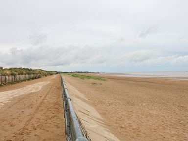 A sandy beach with a rail fence separating a sandy path from the beach at 98 Cherry Park in Chapel St Leonards