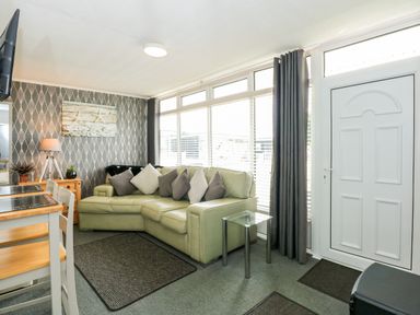 A living room with a sectional sofa dining table and chairs and large windows at 98 Cherry Park in Chapel St Leonards