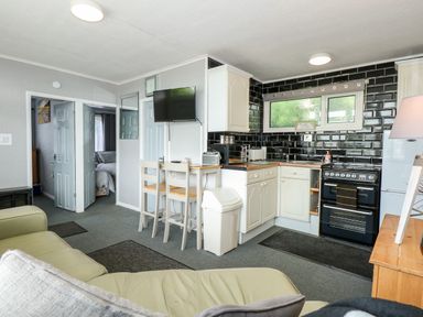 A kitchen and living area with white cabinets black tiled backsplash and a corner stove at 98 Cherry Park in Chapel St Leonards