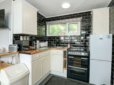 A kitchen with cream cabinets black subway tile backsplash wooden countertops and white appliances at 98 Cherry Park in Chapel St Leonards