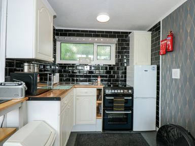A kitchen with white cabinets black tiled walls a refrigerator oven and a window at 98 Cherry Park in Chapel St Leonards