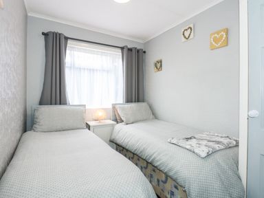 A bedroom with two single beds a small bedside table with a lamp and heart decorations on the wall at 98 Cherry Park in Chapel St Leonards
