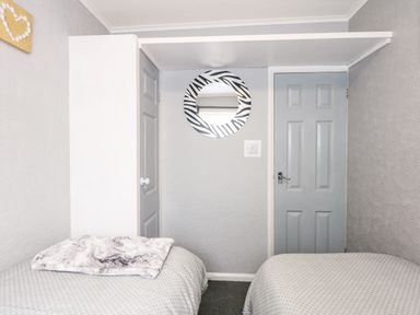 A bedroom with two single beds a round zebra patterned mirror and two grey doors at 98 Cherry Park in Chapel St Leonards